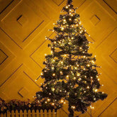 Decorated Christmas tree with lights against a yellow wall